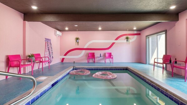 A pool area with pink chairs, a pool with a blue border, and a wall with a large white and red design. - Pink Pines by Avantstay Luxury Aesthetic Dream Home, Indoor Pool, Hot Tub (Sevierville)