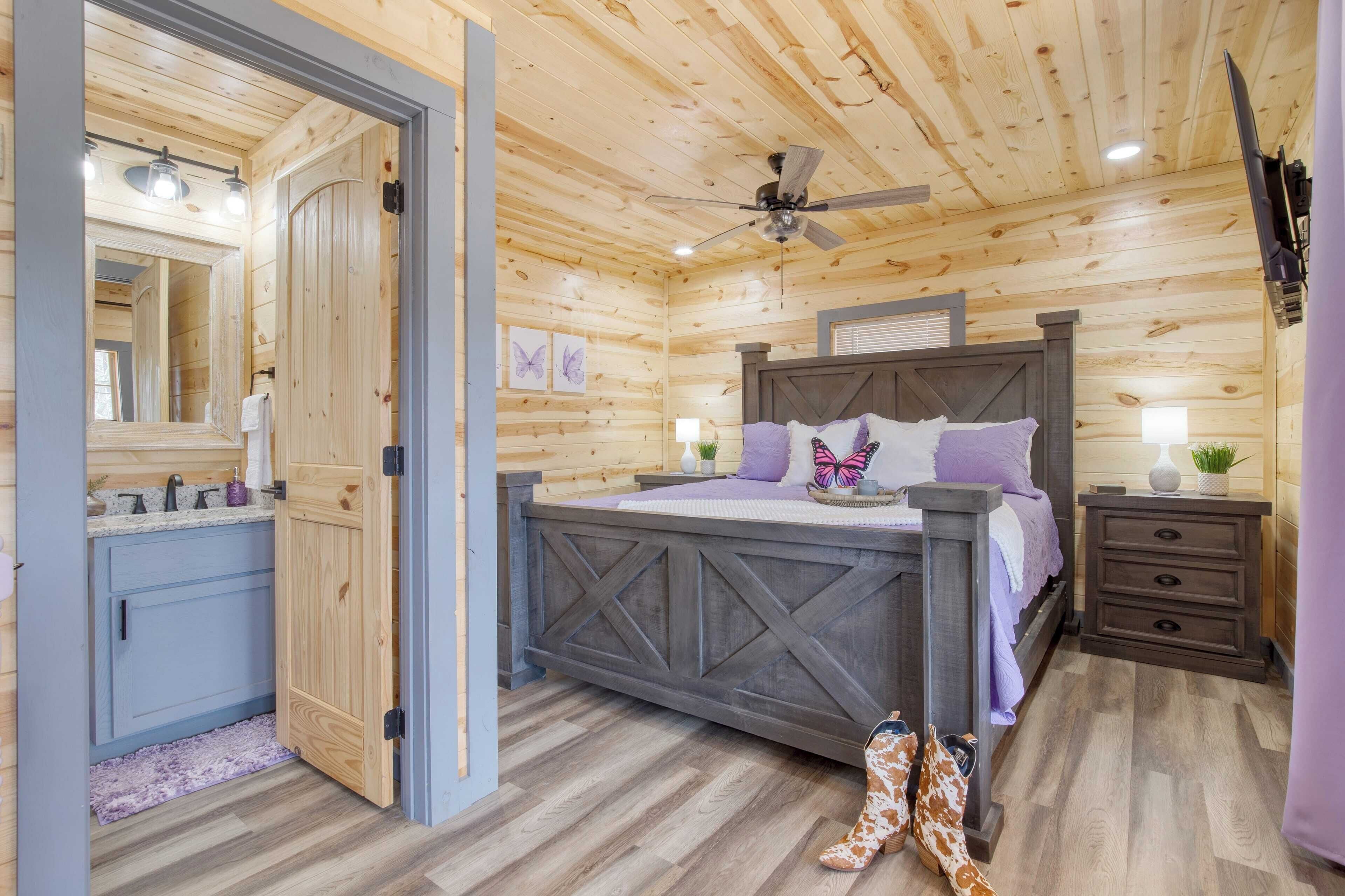 A wooden cabin bedroom with a bed, nightstand, dresser, and a ceiling fan.