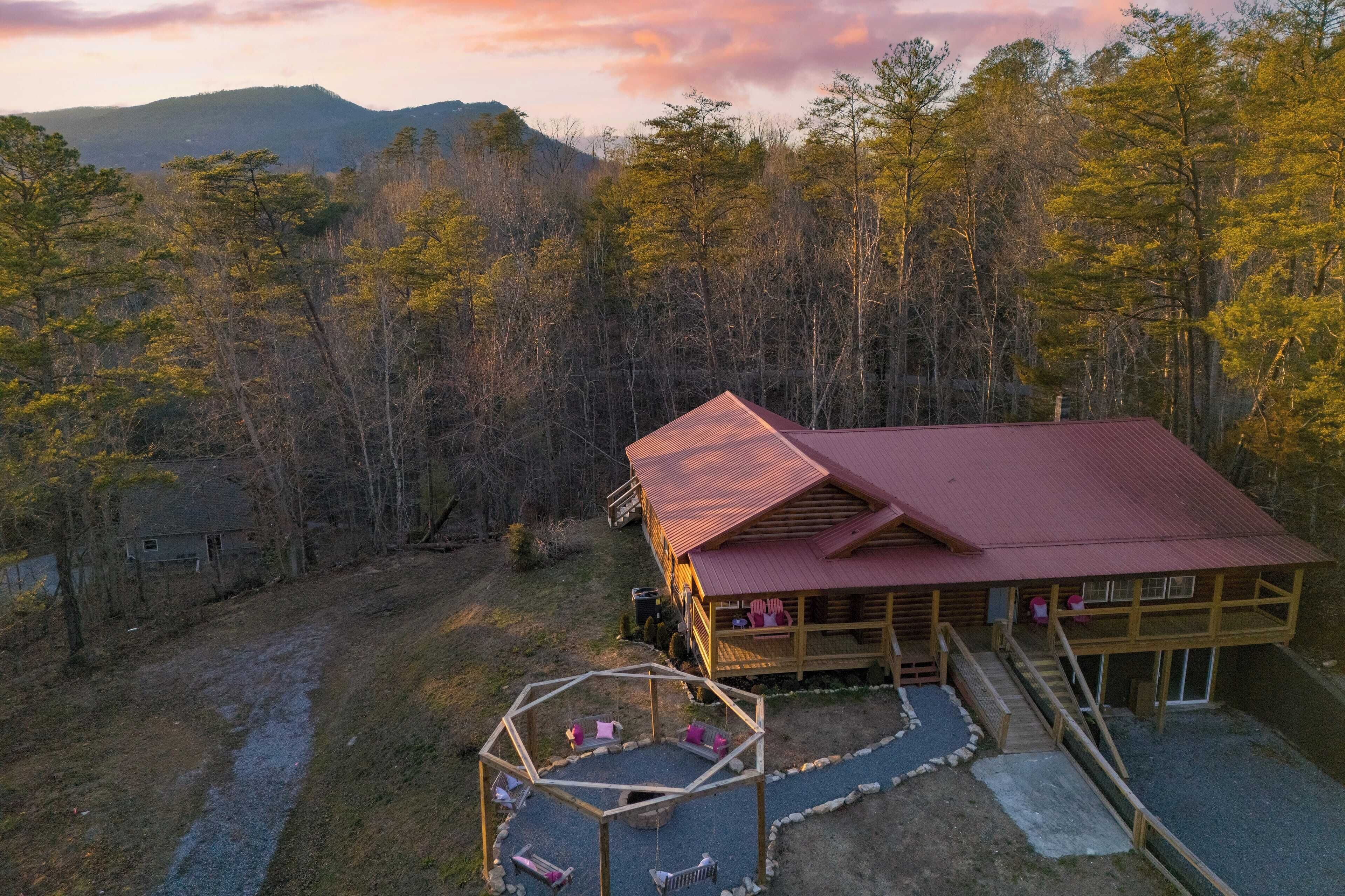 A cabin with a red roof, a covered deck, and a view of surrounding forest and mountains.