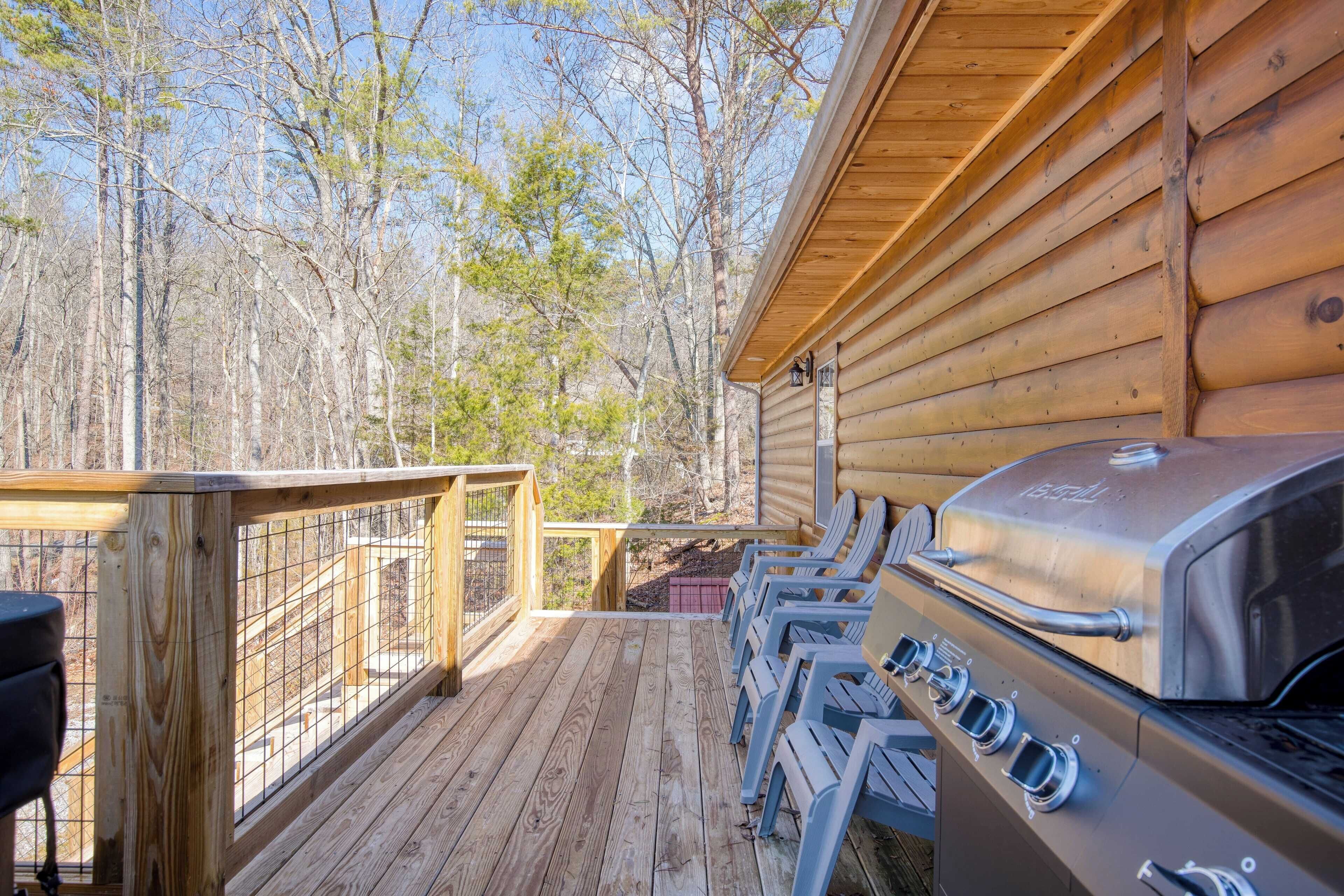 Une terrasse en bois avec un barbecue et des chaises, donnant sur une zone boisée.