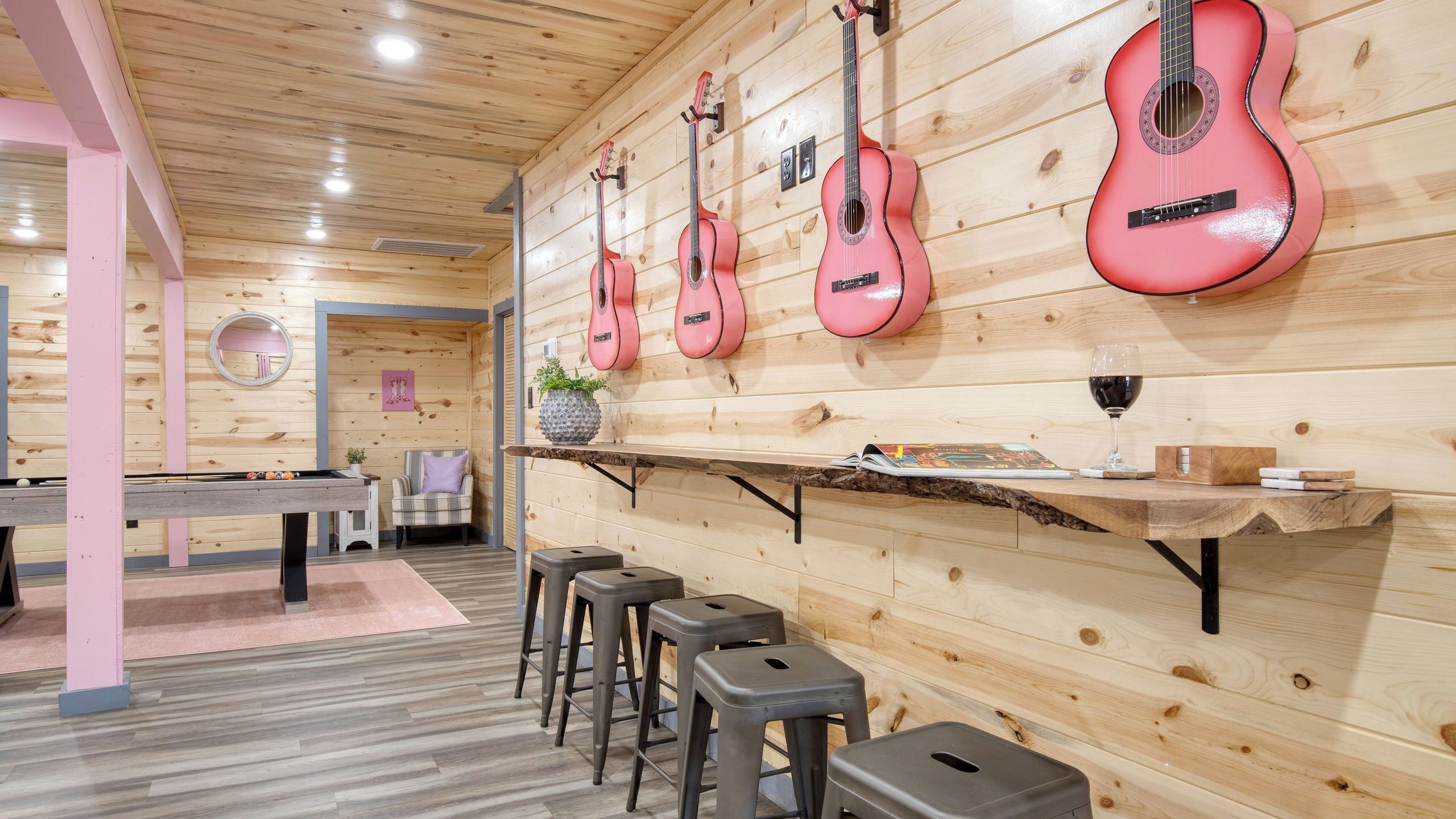 A wooden interior with a pool table, bar area, and multiple guitars on the wall.