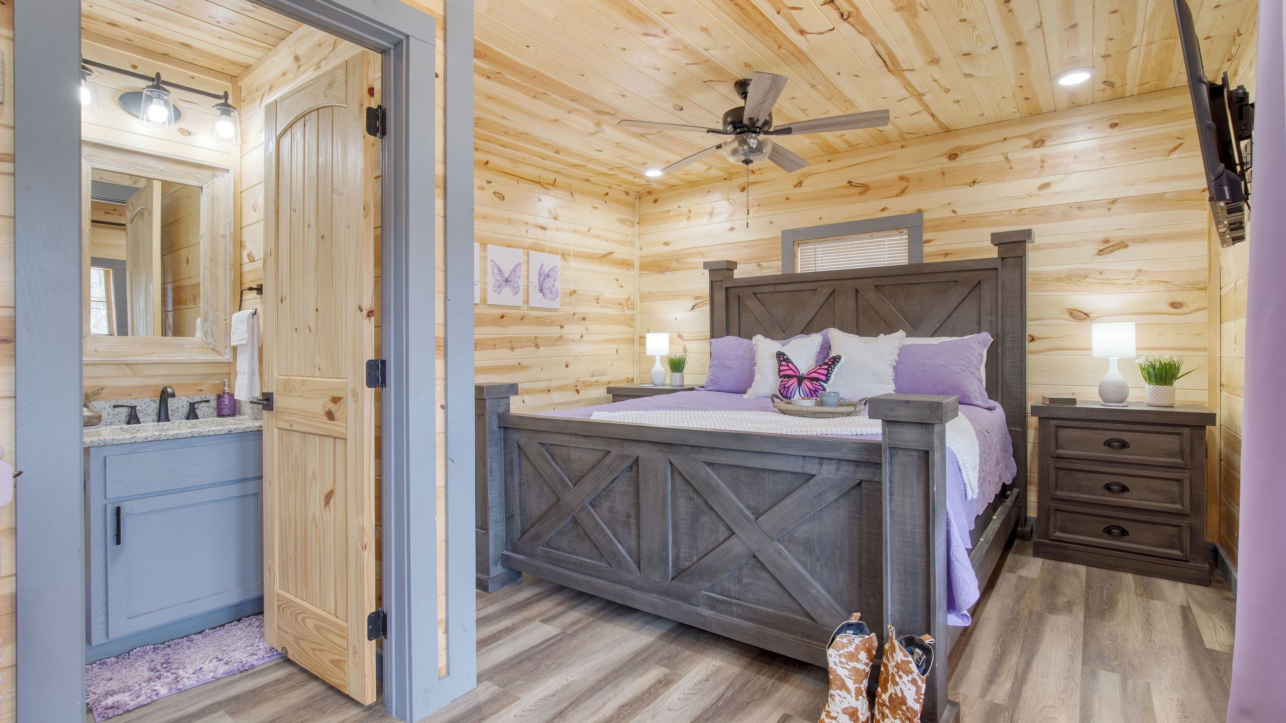 A wooden cabin interior with a bed, bedside table, lamp, and a mirror.