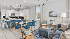 A modern kitchen with white cabinets, a central island, and blue chairs. - Tidal Charm by Avantstay Walk to Beach, Community Pool, Balcony, Ocean Views (Panama City Beach)