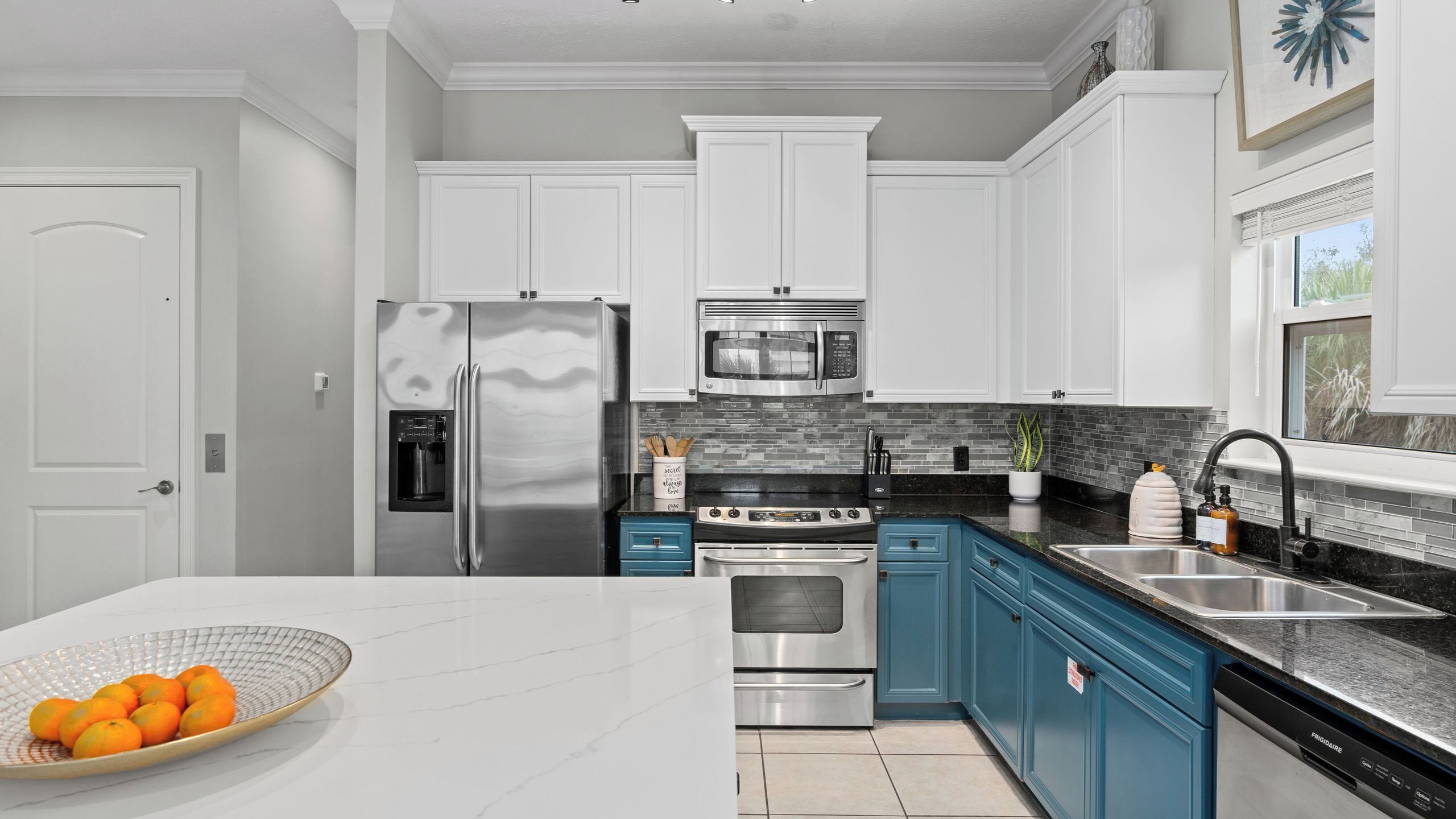 A modern kitchen with white cabinets, stainless steel appliances, a black countertop, and a blue accent wall.
