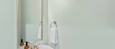 Un baño con un lavamanos blanco, un espejo, un perchero para toallas y un dispensador de jabón.