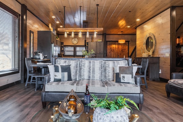 Un salón acogedor con sofá, mesa de comedor y sillas, suelos de madera y un espejo grande en la pared.