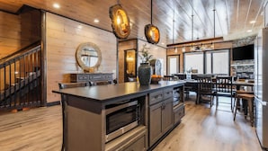 A modern kitchen with a large island, wooden flooring, and a stone fireplace. - Sleeps 18 Luxury Lodge w/ Indoor Pool, Theater, Hot Tub, Game Room Elk Pass (Sevierville)