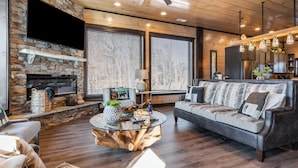 A modern living room with a stone fireplace, a round glass coffee table, a leather sofa, and a ceiling fan. - Sleeps 18 Luxury Lodge w/ Indoor Pool, Theater, Hot Tub, Game Room Elk Pass (Sevierville)