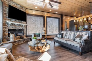 A modern living room with a stone fireplace, a round glass coffee table, a leather sofa, and a ceiling fan. - Sleeps 18 Luxury Lodge w/ Indoor Pool, Theater, Hot Tub, Game Room Elk Pass (Sevierville)
