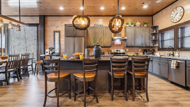 A modern kitchen with wooden cabinets, a central island with bar stools, pendant lighting, and a clock on the wall. - Sleeps 18 Luxury Lodge w/ Indoor Pool, Theater, Hot Tub, Game Room Elk Pass (Sevierville)