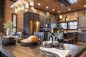 Un interior de madera con una mesa de comedor lista para una comida, armarios de cocina y un reloj en la pared.