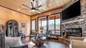 A cozy living room with a stone fireplace, comfortable seating, and large windows. - Sleeps 18 Luxury Lodge w/ Indoor Pool, Theater, Hot Tub, Game Room Elk Pass (Sevierville)