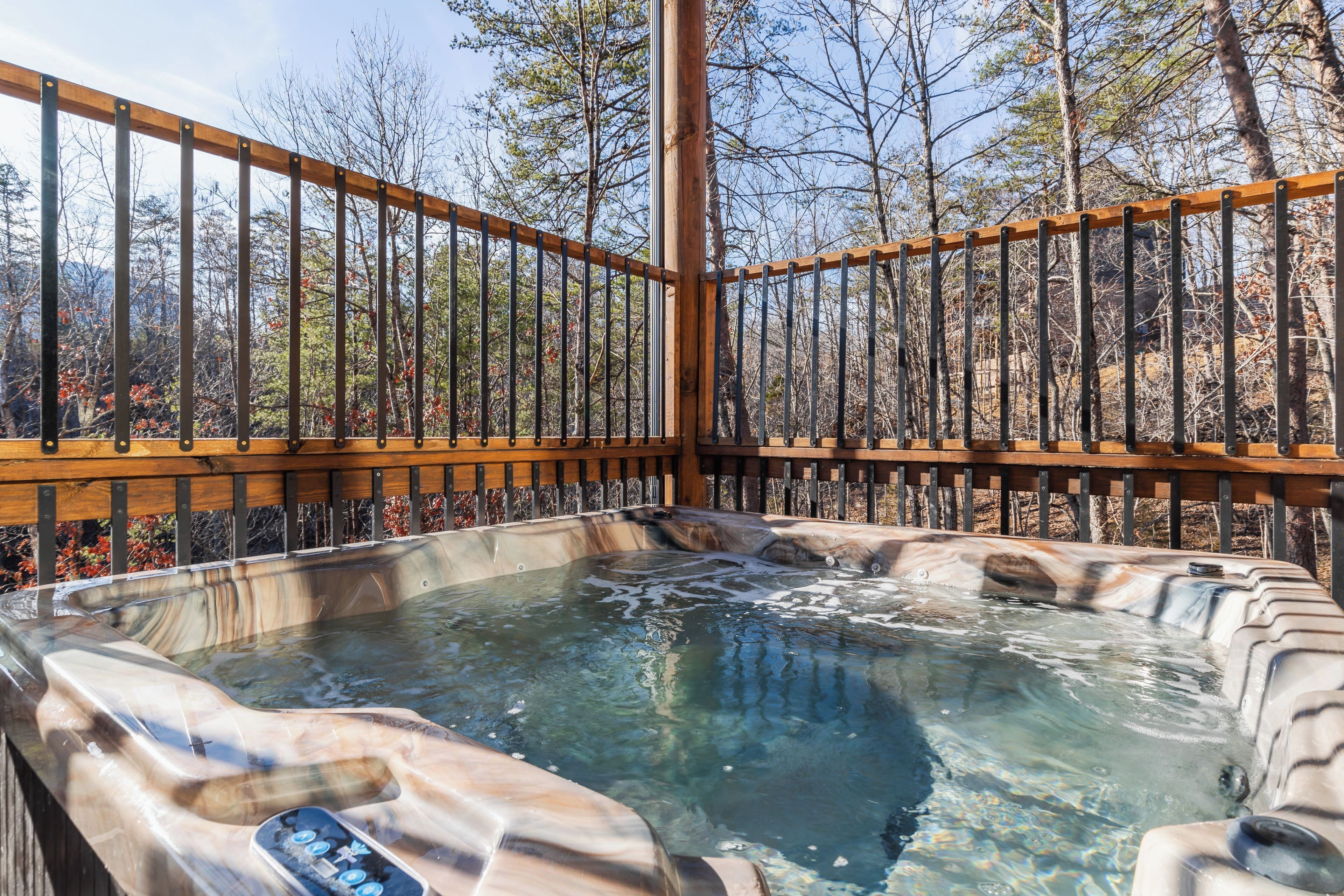 A hot tub with a wooden deck and metal railing, surrounded by trees.