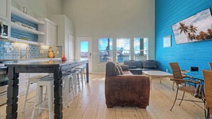 Una cocina moderna con una barra, una sala de estar con un sofá marrón y un comedor con sillas de mimbre.