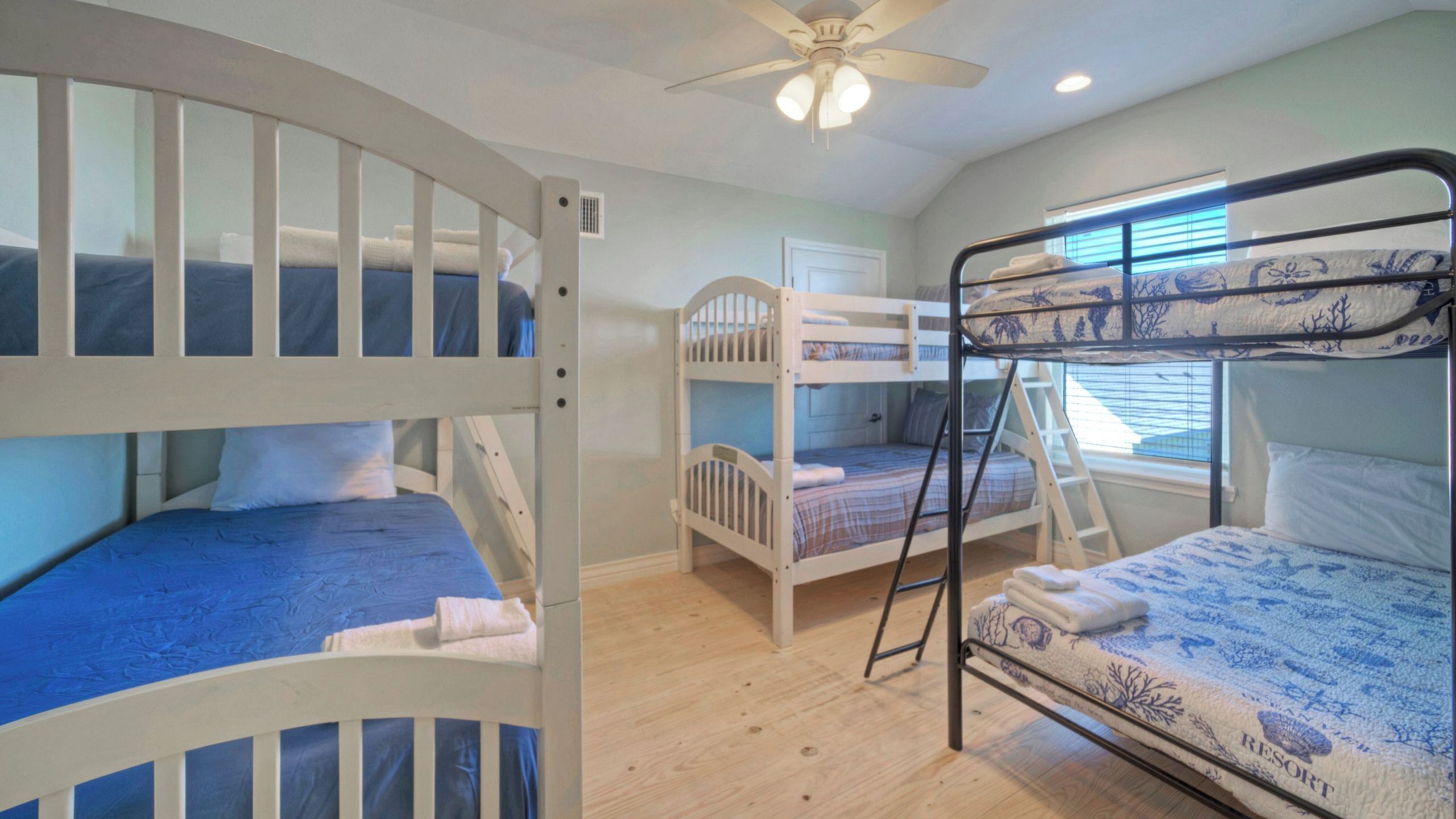 A room with bunk beds, a ceiling fan, and a window with blinds.