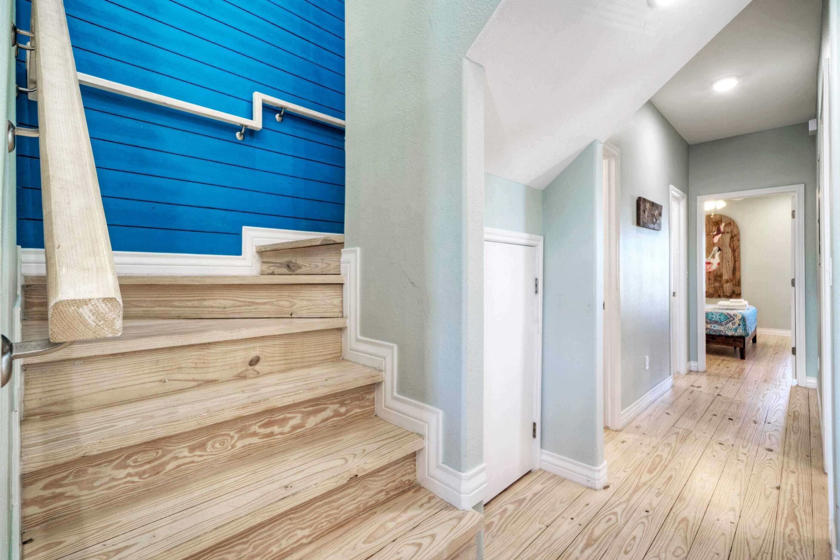 A staircase with wooden steps and a blue wall, leading to a room with a bed and a wooden headboard.