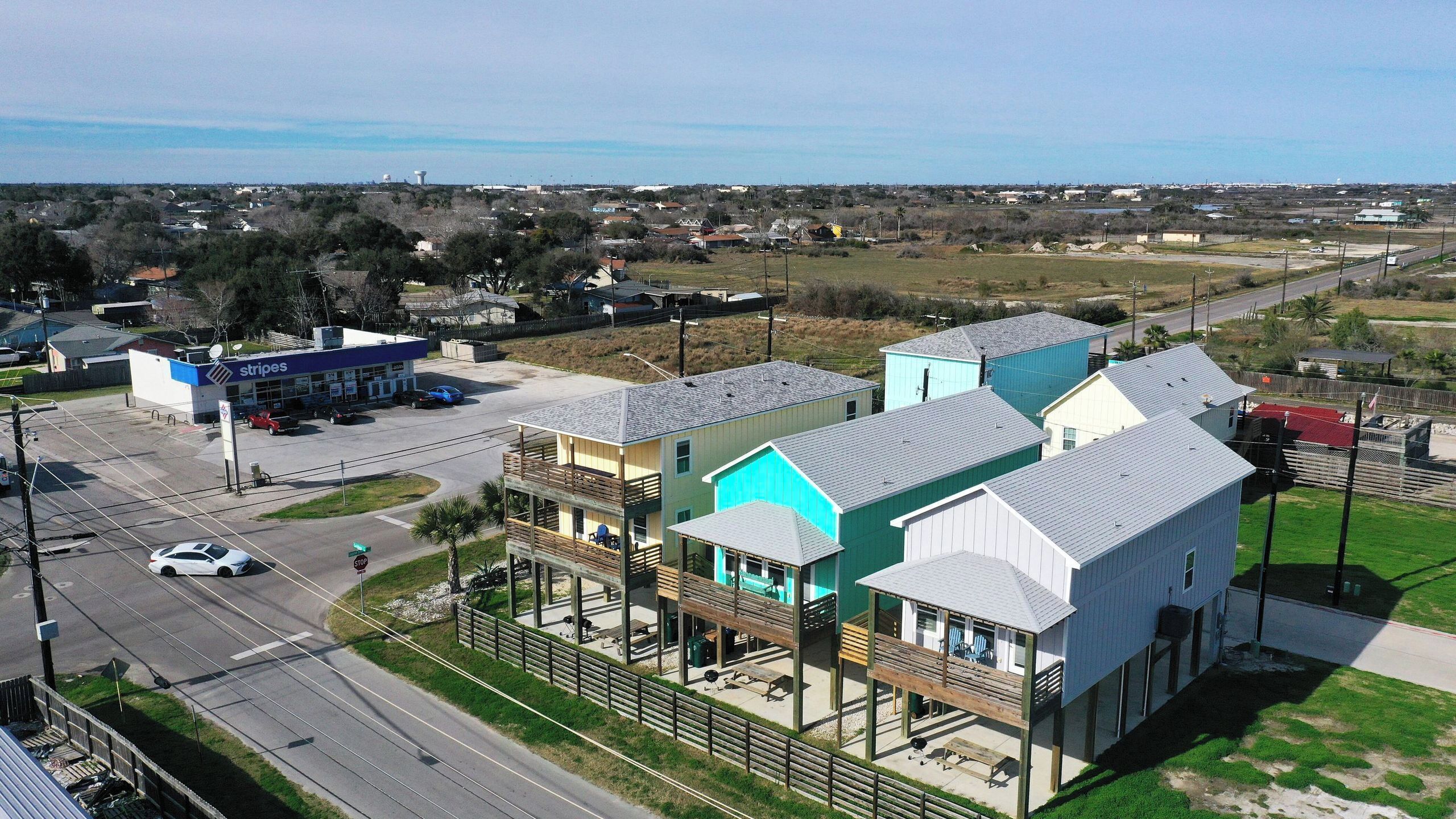 A multi-story building with a commercial strip on the ground floor, a parking lot, and a view of a residential area in the background.