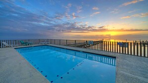 Piscina con valla de madera y sillas de descanso, rodeada de una vista panorámica al atardecer.