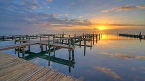 Un muelle de madera que se adentra en aguas tranquilas con un atardecer al fondo.