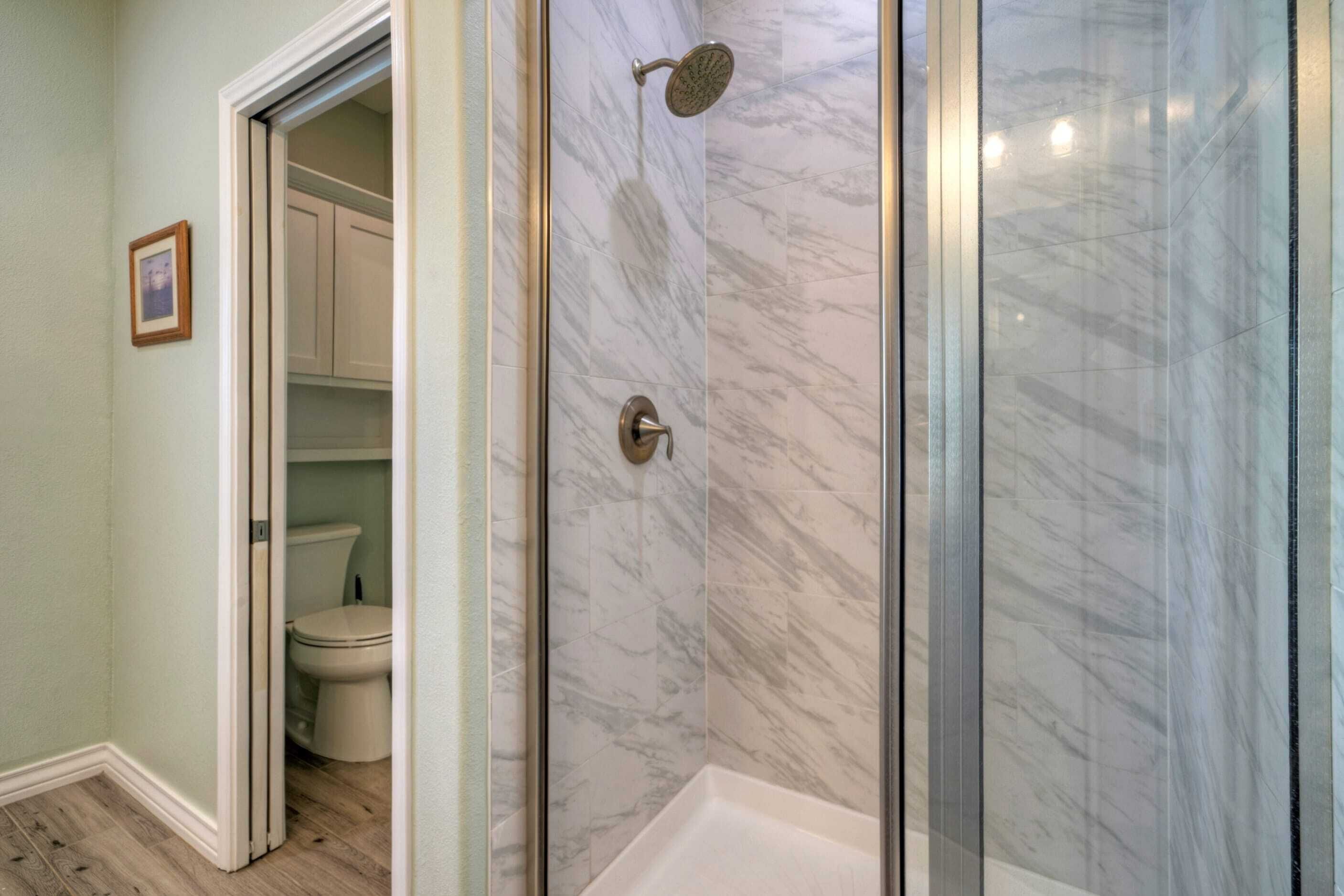 A bathroom with a glass-enclosed shower, a toilet, and a cabinet.