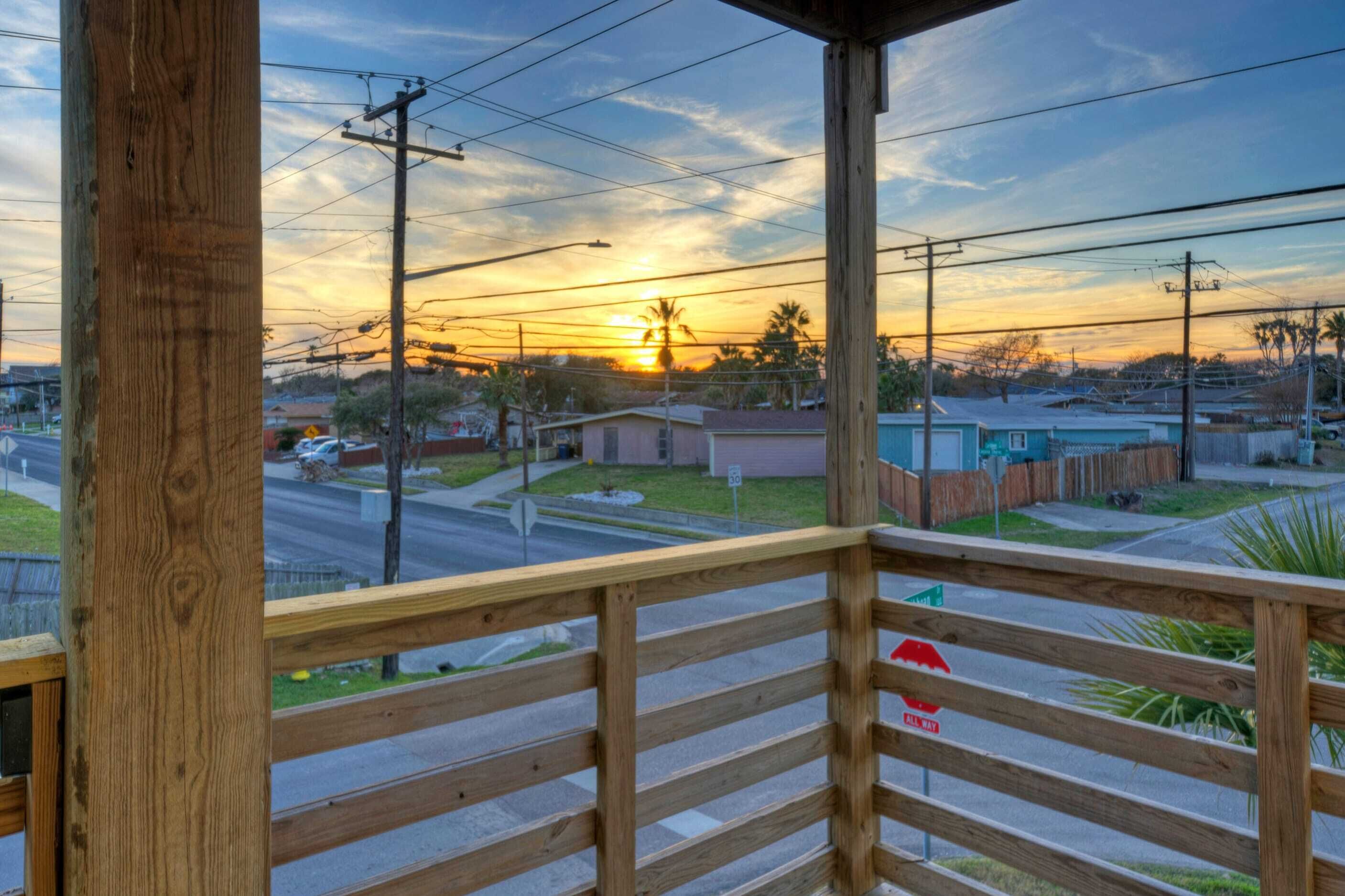 A wooden balcony with a view of a street and sunset.