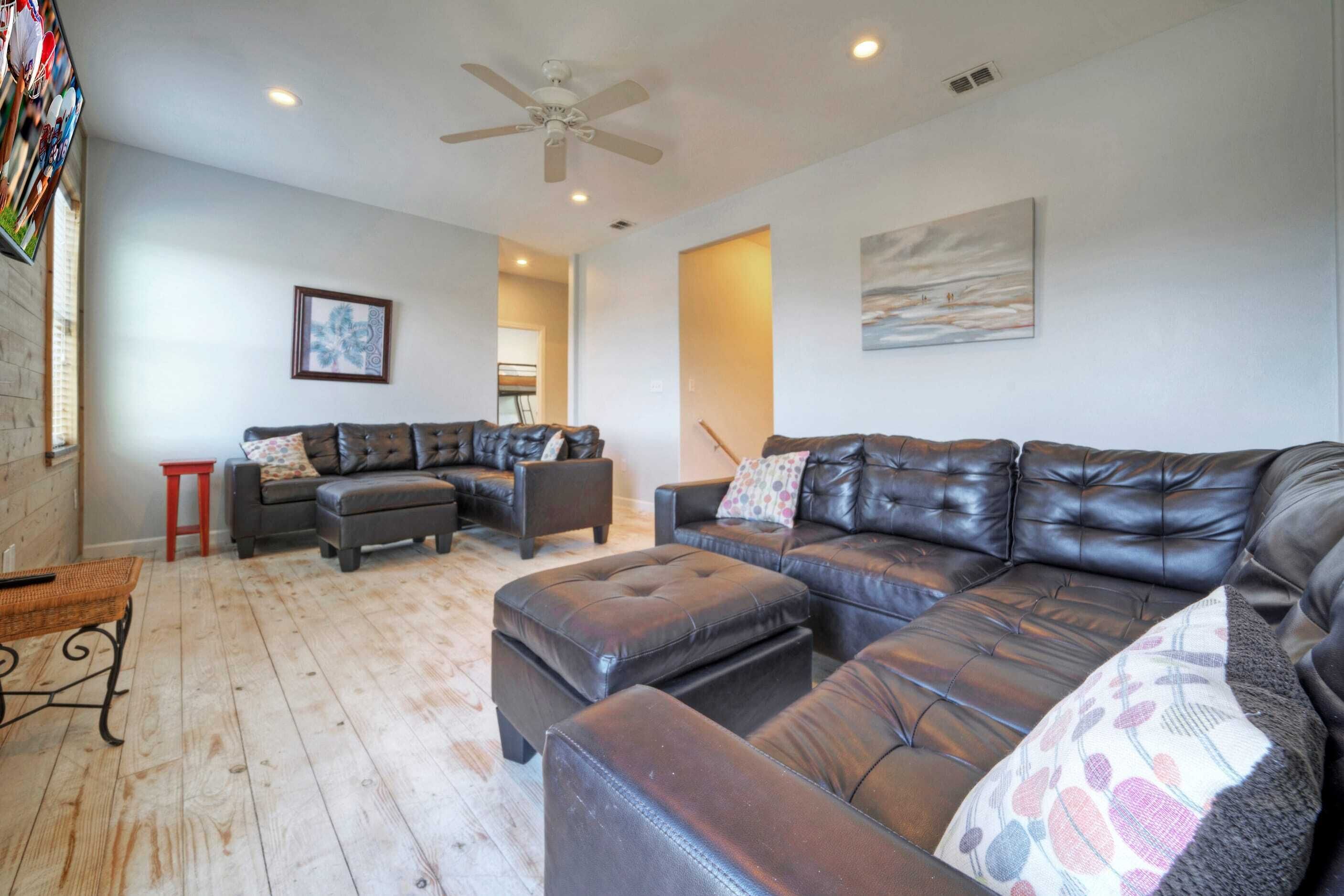 A spacious living room with a large sectional sofa, a small table, and a ceiling fan.