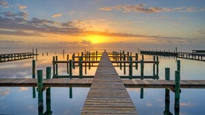 A wooden pier extending into calm waters with a sunset in the background. - 6bdr, Balcony w/ Bay View, Shared Pool + Boat Dock Keeper Red by Avantstay (Corpus Christi)