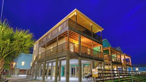A waterfront property with a multi-level wooden deck, a covered outdoor area, and a visible entrance. - 6bdr, Balcony w/ Bay View, Shared Pool + Boat Dock Keeper Red by Avantstay (Corpus Christi)