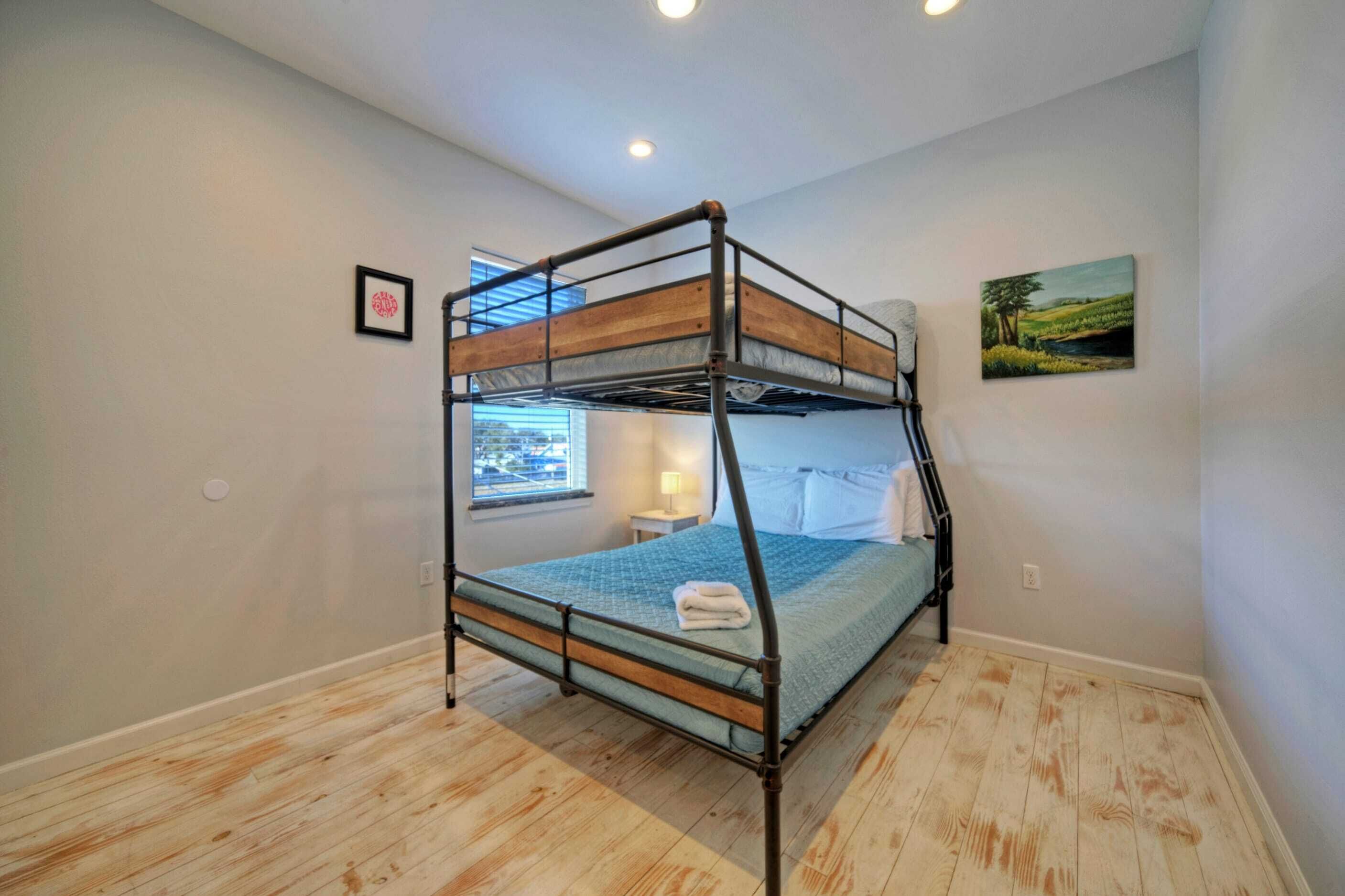 A bunk bed room with a window, a painting on the wall, and a small bedside table with a lamp.