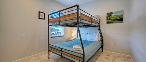 A bunk bed room with a window, a painting on the wall, and a small bedside table with a lamp.