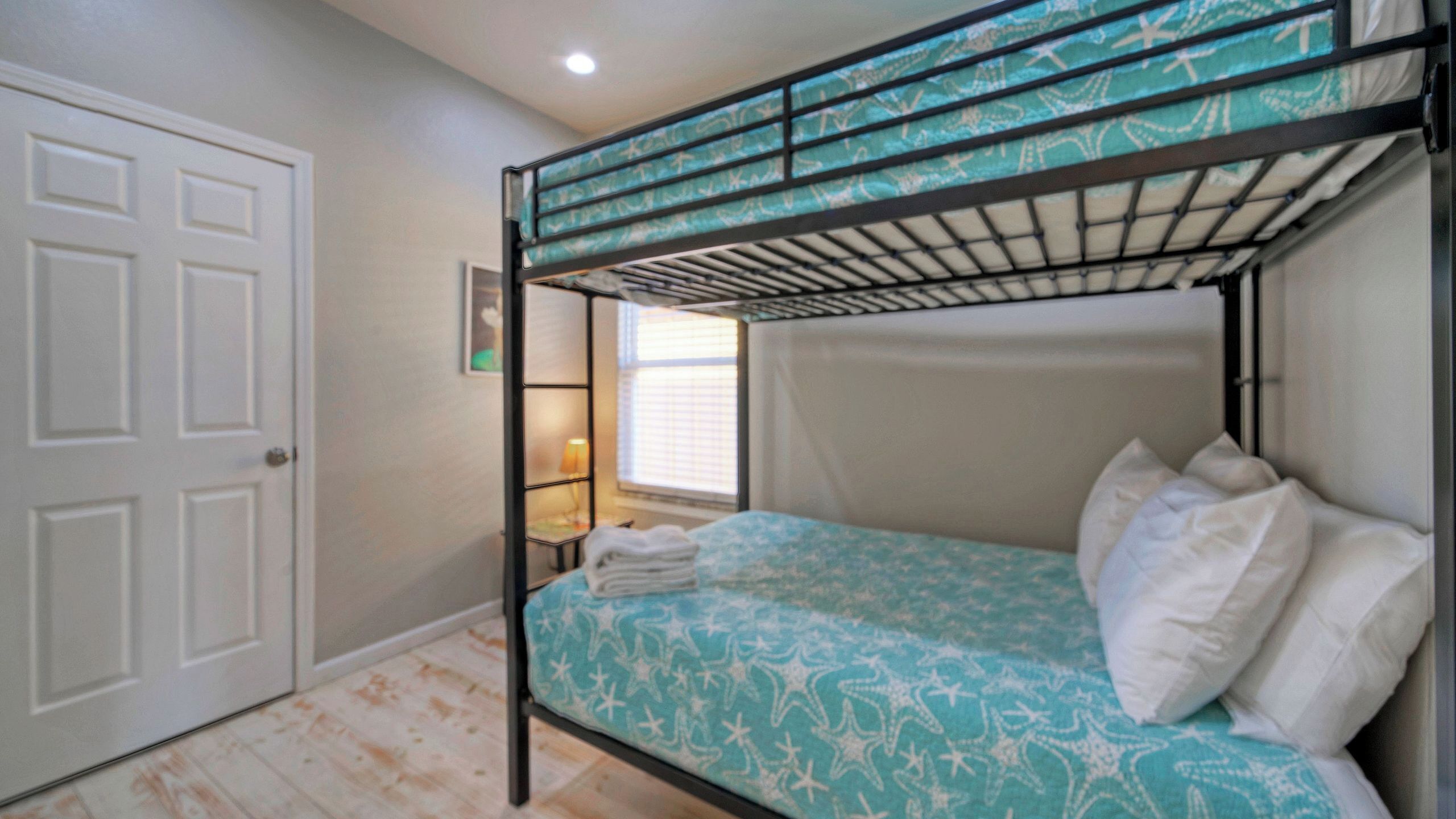 A bunk bed with a patterned bedspread, a bedside table with a lamp, and a door.