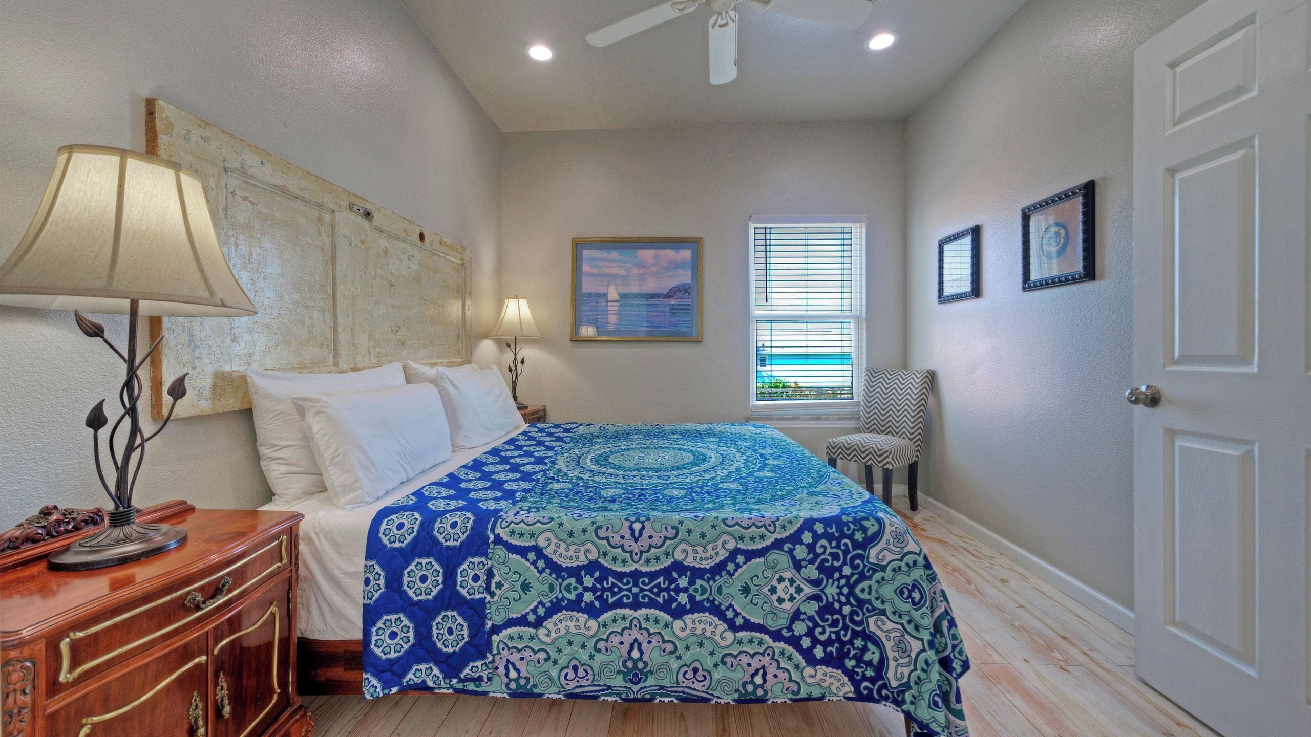 Un dormitorio con cama, mesita de noche, silla, ventana con persianas y puerta.