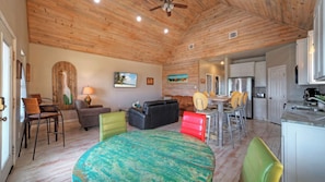 A rustic interior with a wooden ceiling, a dining area, a kitchen, and a living room with a round table and chairs. - Bay Haven w/ Shared Boat Dock & Waterfront Pool Big Trout by Avantstay (Corpus Christi)