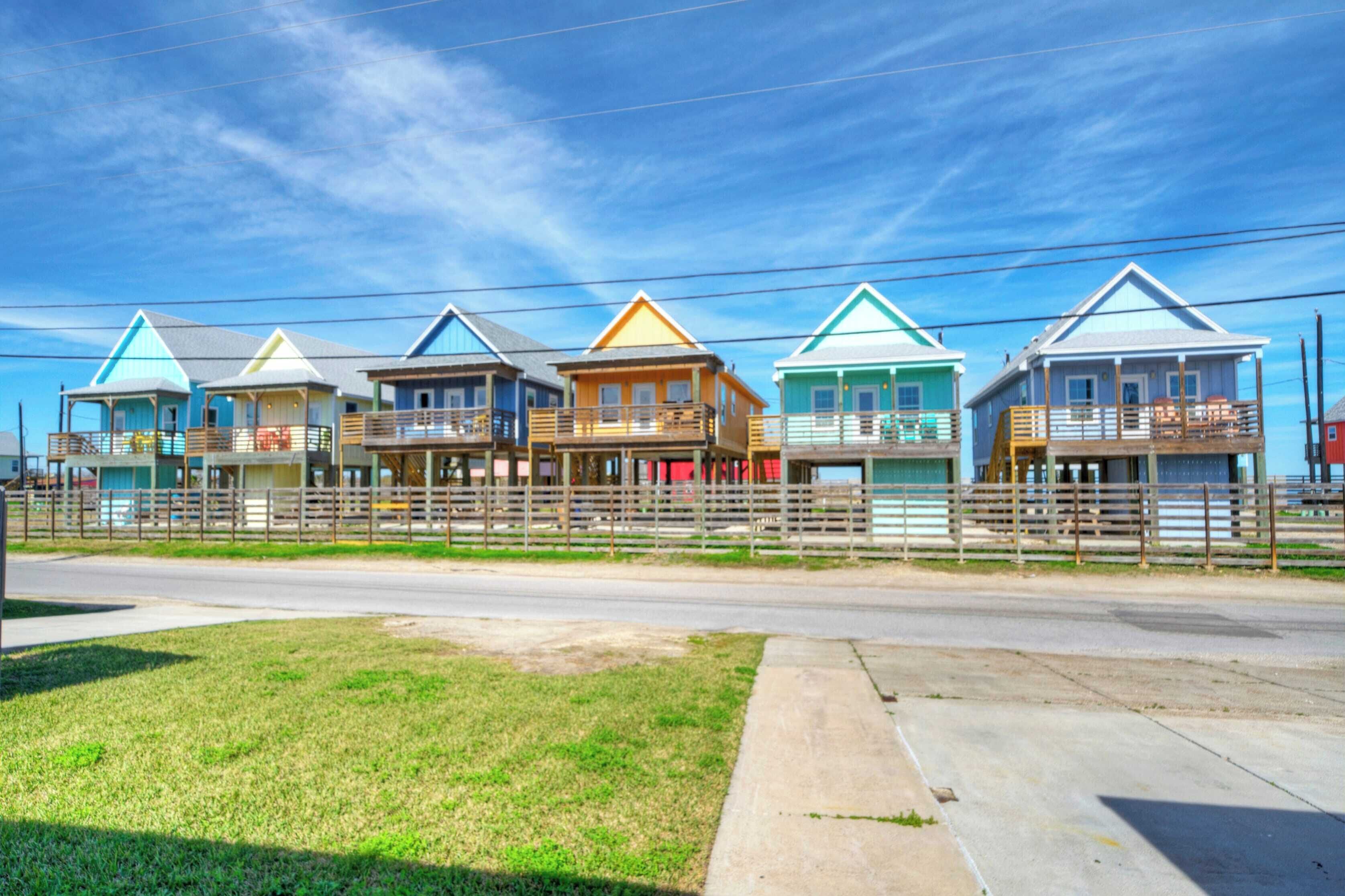 A row of colorful beach houses with balconies, a wooden fence, and a clear sky.