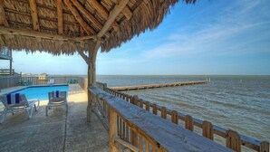 Zona de piscina amb gandules, un pont de fusta i vista a l'oceà.
