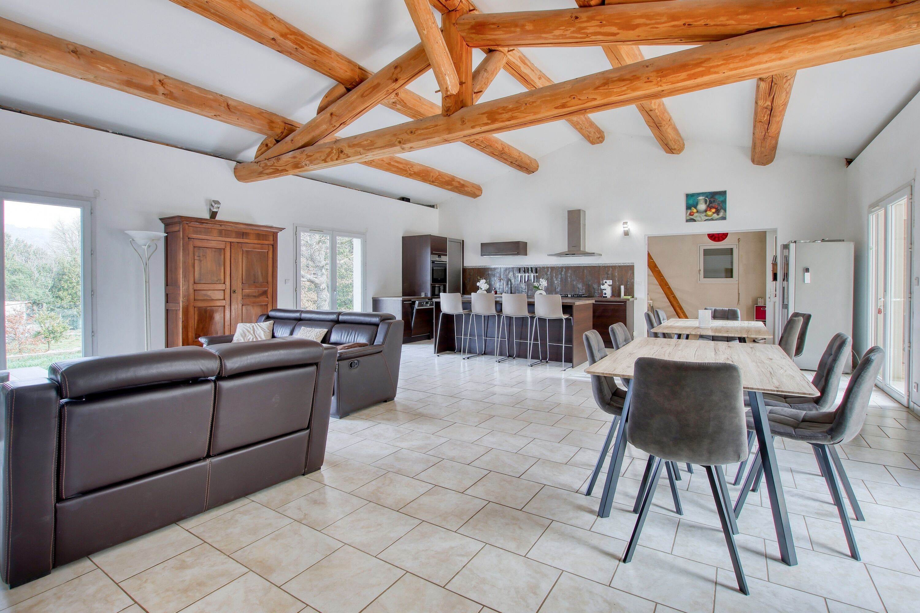 Un vaste espace de vie comprenant un canapé en cuir marron, une table à manger en bois avec des chaises, et une cuisine en arrière-plan.