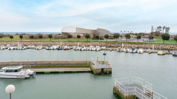 Un port de plaisance avec des bateaux amarrés, un grand bâtiment en arrière-plan et un ciel dégagé.