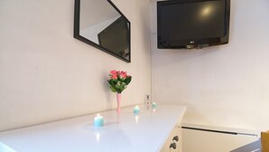 Una encimera blanca con un florero rosa, tres velas color turquesa y un televisor de pantalla plana montado en la pared.