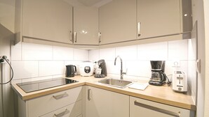 Una cocina moderna con armarios blancos, un lavamanos de acero inoxidable y diversos electrodomésticos, incluyendo una cafetera y un tostador.