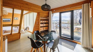 Interior de madera con una mesa de comedor de vidrio, sillas negras y vistas a través de un amplio ventanal corredero.