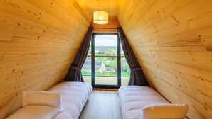Habitación acogedora con paredes de madera y techo inclinado, que incluye dos camas con ropa blanca y un ventanal con cortinas.