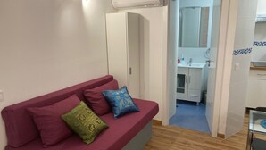 Una habitación con un sofá rojo, una mesita y un baño visible a través de una puerta abierta.