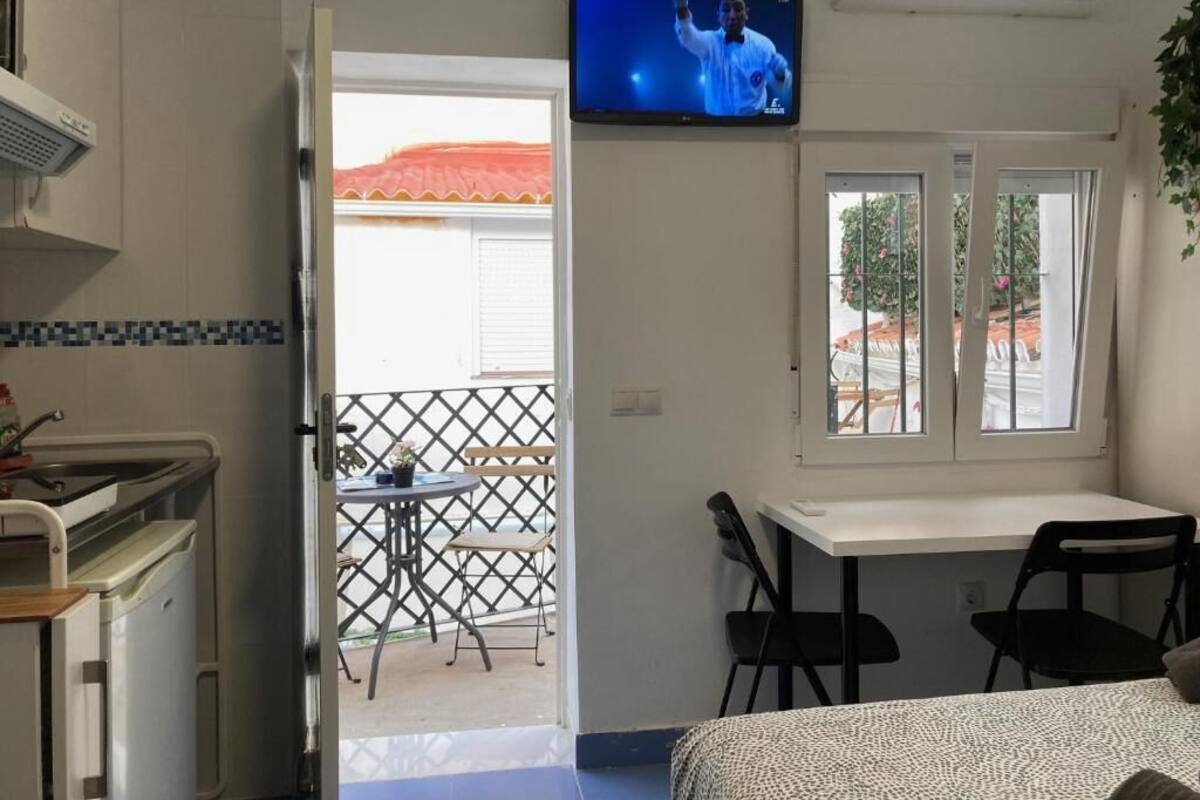 Une chambre dotée d’une kitchenette, d’un téléviseur fixé au mur, d’un balcon avec une table et des chaises, et d’une fenêtre donnant sur l’extérieur.