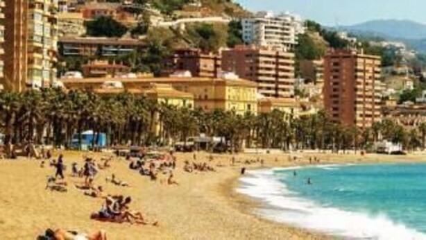 Un paisaje urbano costero con playa, edificios y una montaña al fondo.