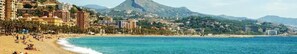Un paisaje urbano costero con playa, edificios y una montaña al fondo.