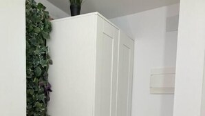 Una habitación pequeña con un armario blanco, una mesa de madera con dos sillas, una planta en maceta y un adorno verde en la pared.