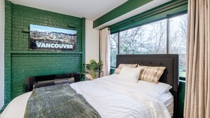 Ein Schlafzimmer mit grüner Ziegelwand, einem Bett mit weißer Bettwäsche, einem großen Fenster mit Vorhängen und einem Stadtplakat an der Wand.