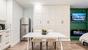 Eine moderne Küche mit weißen Schränken, einem Edelstahlkühlschrank und einem Essbereich mit einem weißen Tisch und zwei Stühlen.