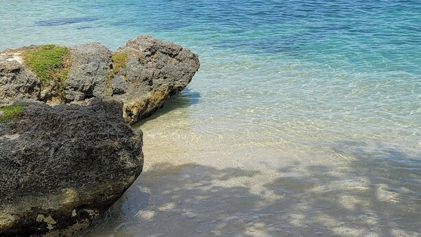 Ein klarer Blick auf einen Strand mit Felsen und einer kleinen Insel im Hintergrund.