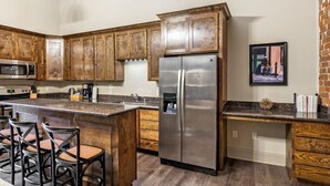 Una cocina con armarios de madera, un refrigerador de acero inoxidable, un microondas y una zona de bar con taburetes.